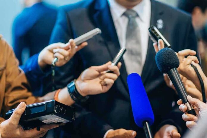 Man in suit surrounded by microphones at press conference