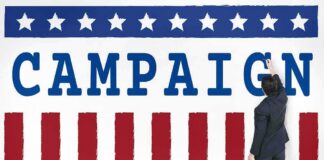 Man in suit writing on large campaign banner with stars and stripes