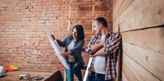 Two people reviewing blueprints in a rustic room under renovation