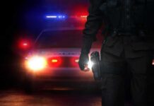 Midnight Break-In: Doctor Down, Motive Missing Police officer stands before patrol car with flashing lights at night