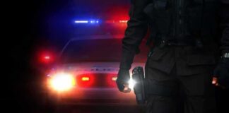 Police officer stands before patrol car with flashing lights at night