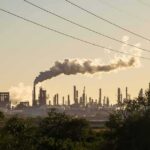 Industrial refinery with smokestack emitting plume at sunset
