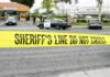 yellow sheriff's line tape blocks a street near police cars