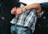 police officer handcuffing person against a car