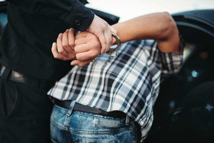 shutterstock_1144500824 police officer handcuffing person against a car