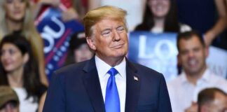 Donald Trump at a rally wearing a dark suit and blue tie