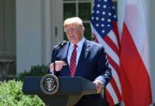 Donald Trump speaking at a podium with U.S. and Polish flags behind him