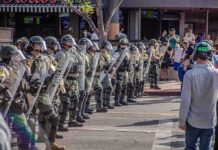 Riot police in helmets and shields form a line on a city street