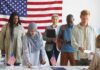 Citizenship? California Shrugs, DOJ Strikes Voters standing in line at a polling station with a U.S. flag
