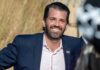 Donald Trump Jr. smiling in a navy suit outdoors