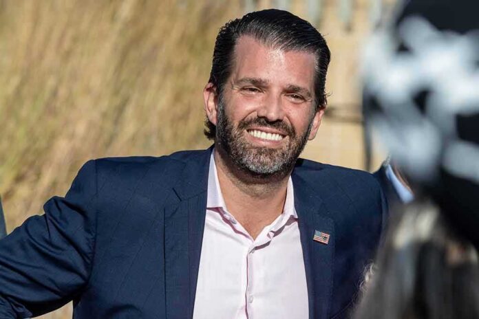 Donald Trump Jr. smiling in a navy suit outdoors