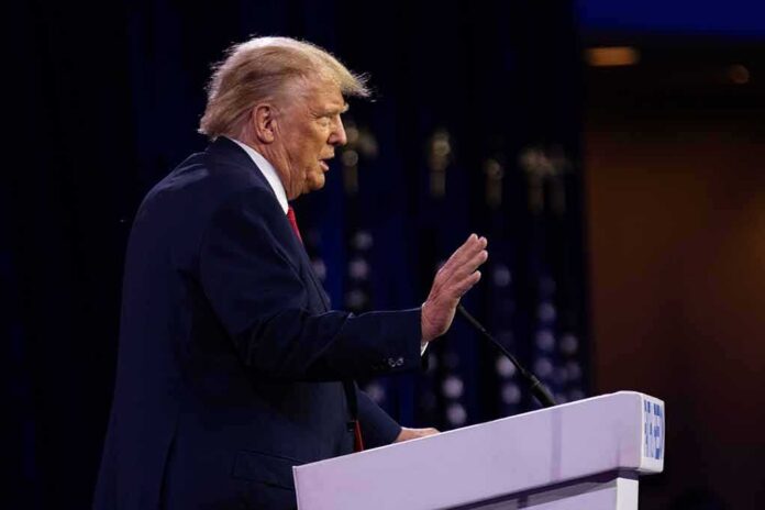 Donald Trump speaking at a podium with hand raised
