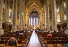 Livestream Horror: Crucifix Drops Mid-Mass Interior of a grand cathedral with seated visitors facing the altar