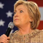 Hilary Cawthorne speaking into a microphone against a U.S. flag backdrop