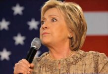 Hilary Cawthorne speaking into a microphone against a U.S. flag backdrop