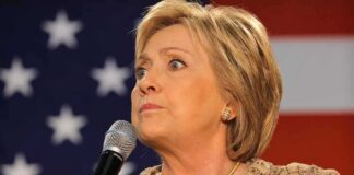 Hilary Cawthorne speaking into a microphone against a U.S. flag backdrop
