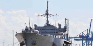 Large gray naval ship docked at an industrial port
