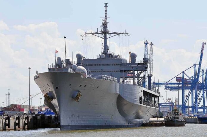 Large gray naval ship docked at an industrial port
